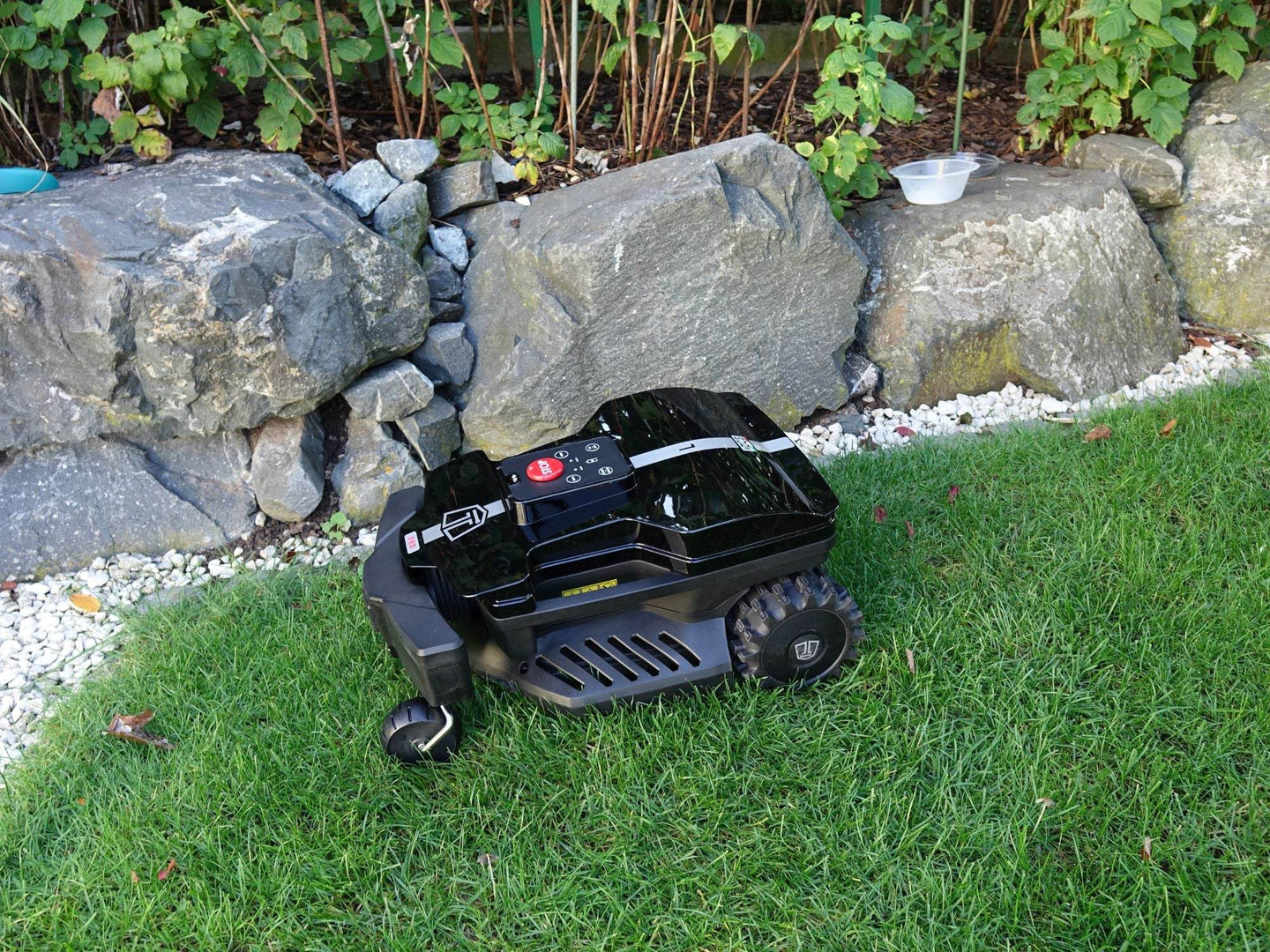 Das Bild zeigt den schwarzen Mähroboter Techline DX25 in einer seitlichen Ansicht von oben, wie er auf einer Wiese steht.