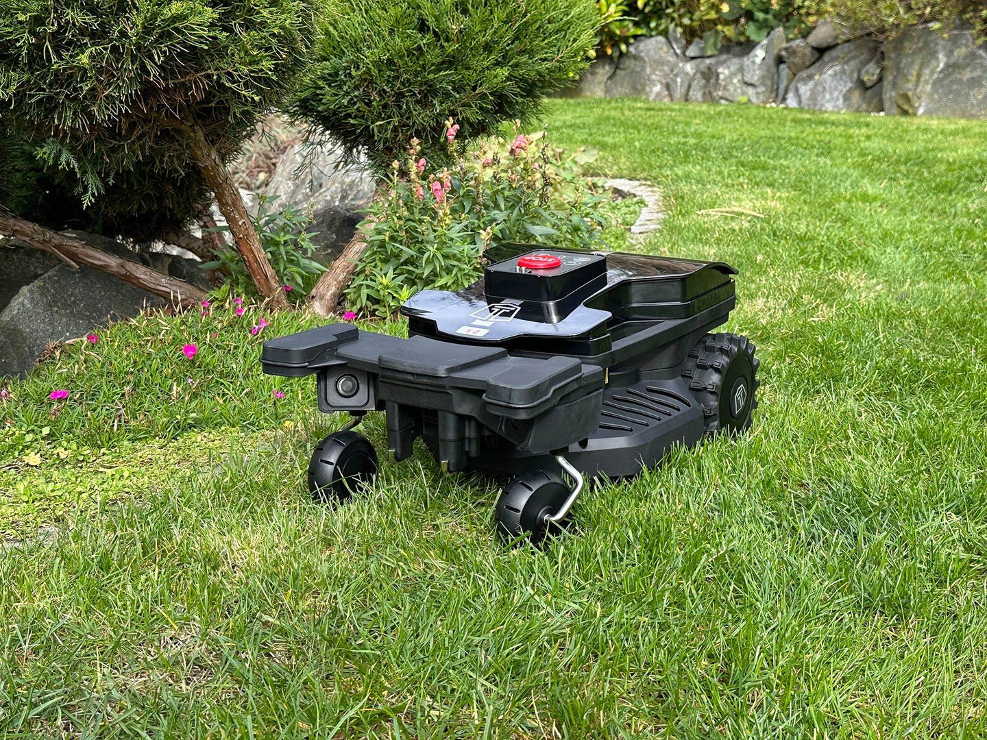 Das Bild zeigt den Mähroboter LX2 ZR EVO in einer Frontalansicht, wie er einen Kreis fährt, während er an Blumen und Büschen entlang arbeitet.