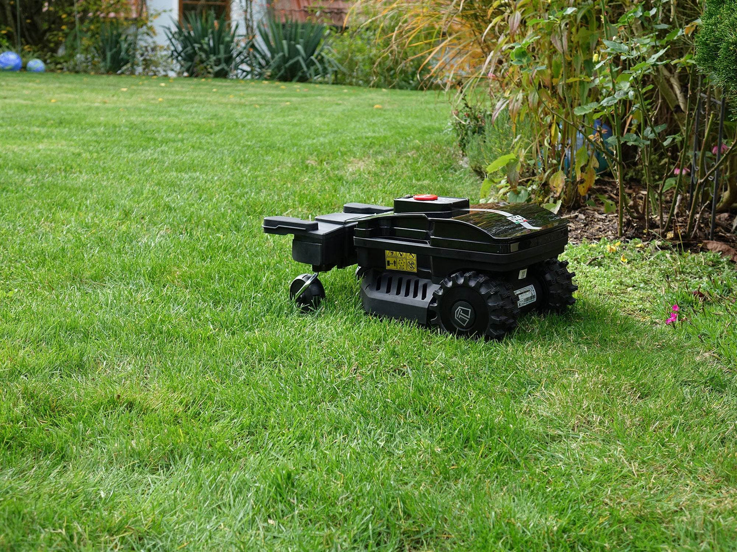 Der schwarze Techline NEXT TECH ZR EVO Mähroboter steht auf einem kurz geschnittenen englischen Rasen. Der Roboter ist von der Seite zu sehen. Er hat oben eine große rote Stopptaste, die den Roboter nach dem Drücken sofort stoppt.