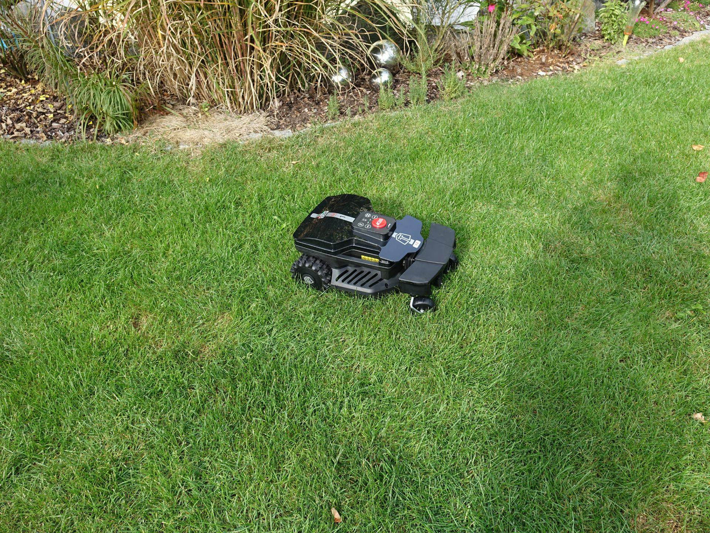 Das Bild zeigt den schwarzen Mähroboter Techline ZR aus der Vogelperspektive, wie er auf einer Gartenwiese steht. Die Gartenwiese, auf der der Mähroboter steht, unterstreicht seine Funktionalität und harmonische Integration in die Umgebung.