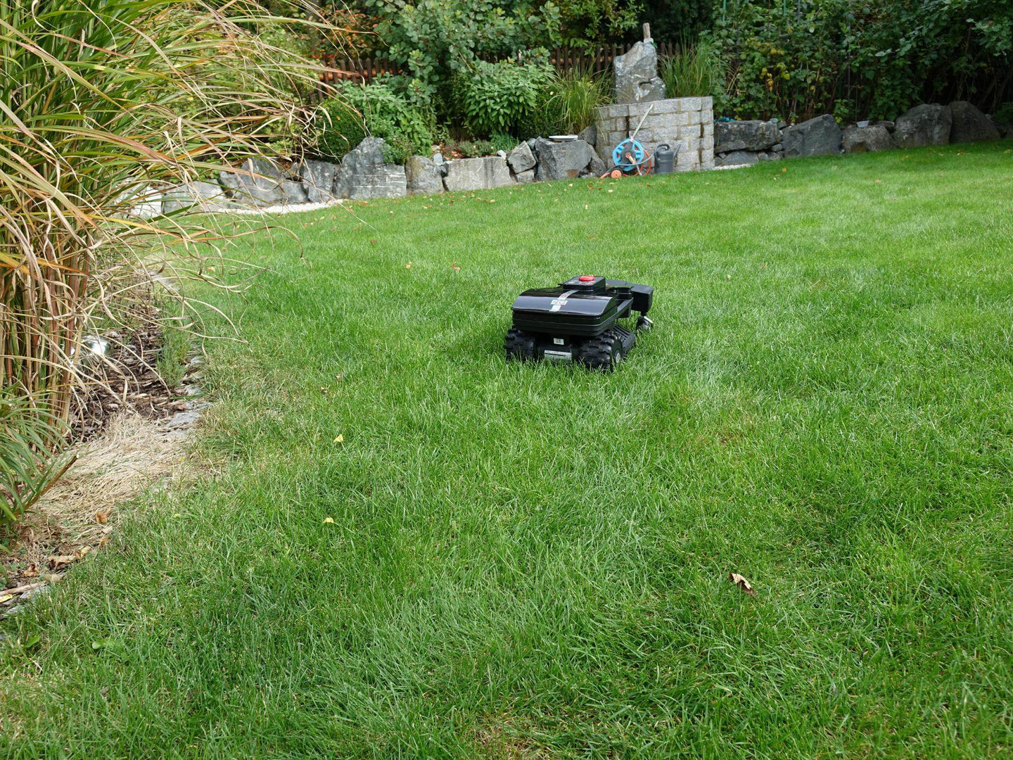 Das Bild zeigt den schwarzen Mähroboter Techline ZR in einer hinteren Ansicht, wie er auf einer Gartenwiese steht.