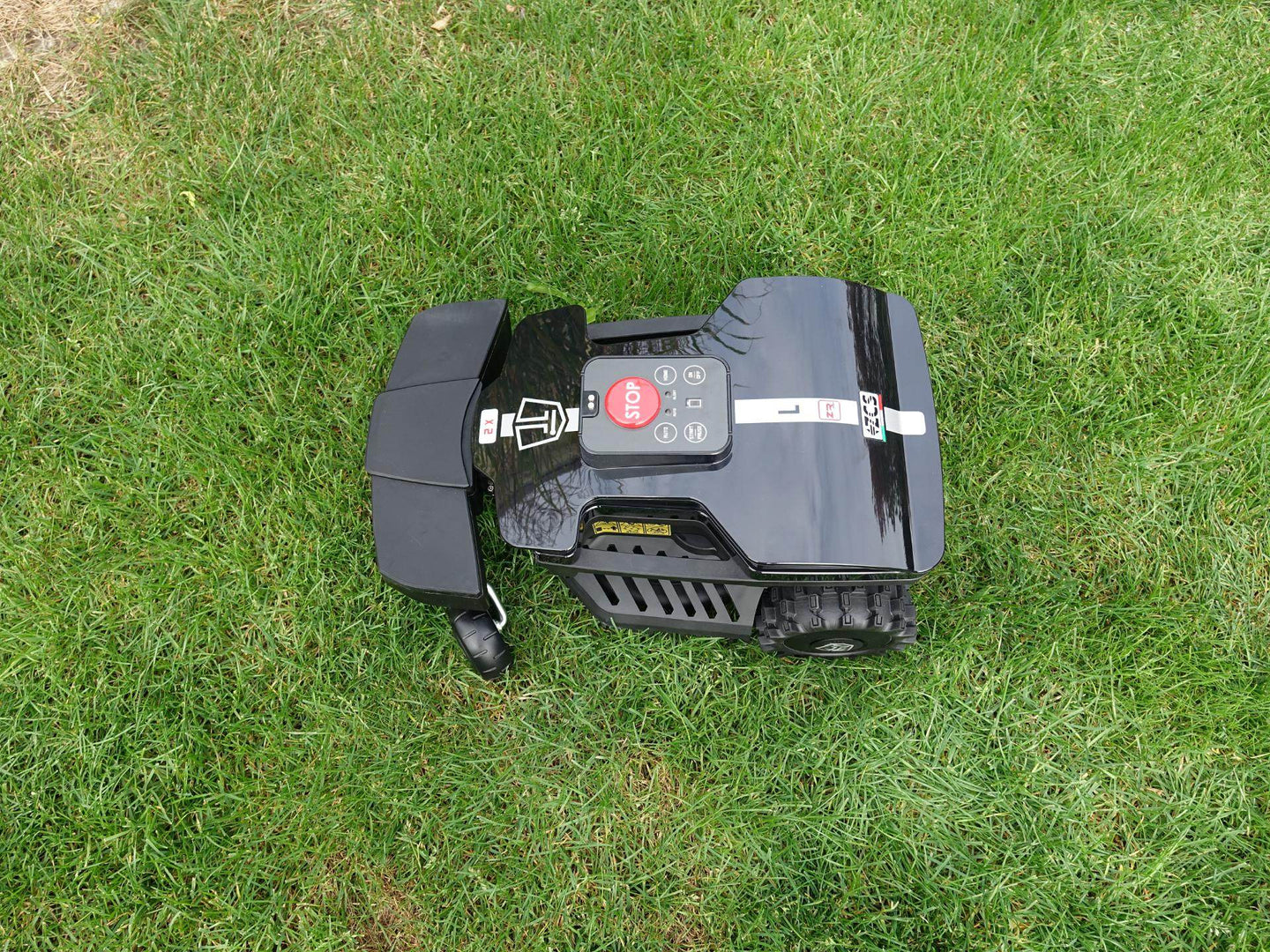 Das Bild zeigt den schwarzen Mähroboter Techline ZR aus der Vogelperspektive, wie er auf einer Gartenwiese steht. Gut zu sehen ist die rote Start-Stop-Taste und die anderen Tastatur-Knöpfe.