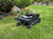 Das Bild zeigt den Mähroboter LX2 ZR EVO in einer Frontalansicht, wie er einen Kreis fährt, während er an Blumen und Büschen entlang arbeitet.