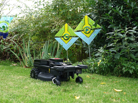 Das Bild zeigt den Mähroboter von vorne, wie er vor einem großen Busch positioniert ist.