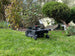 Das Bild zeigt einen schwarzen Techline NEXT TECH ZR EVO Mähroboter in der Frontansicht. Im Hintergrund sind Sträucher zu sehen.
