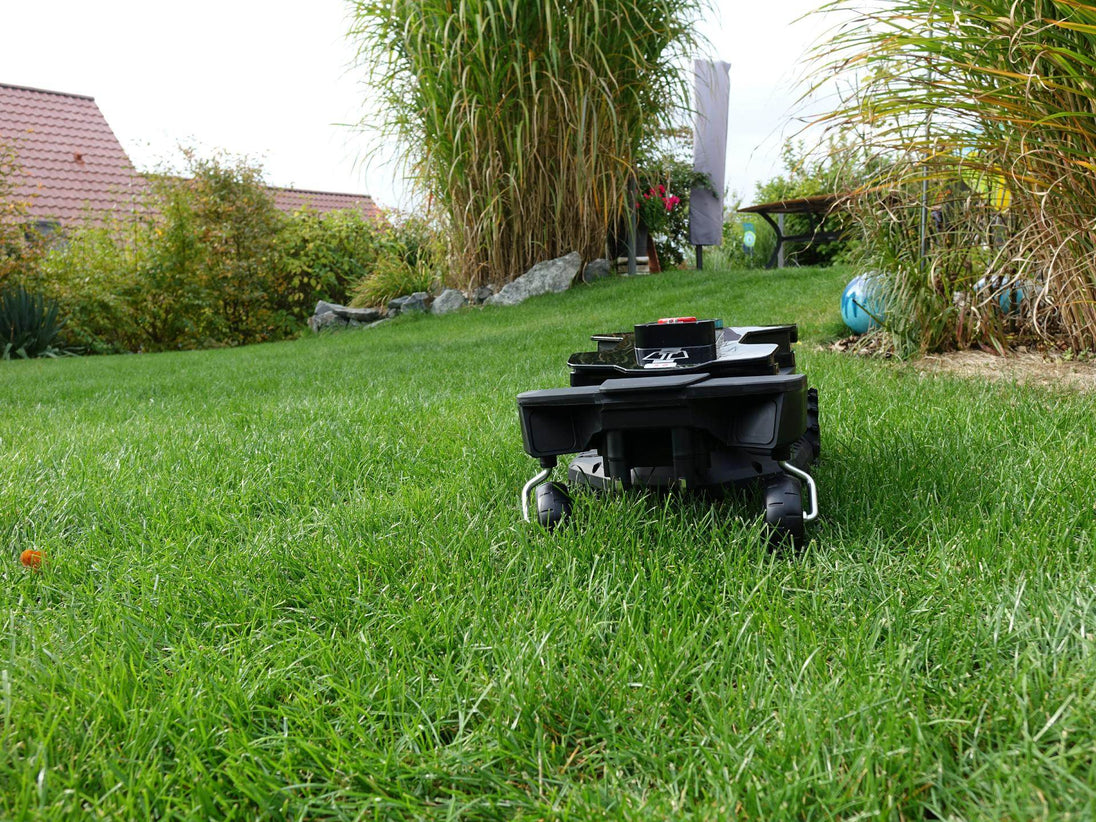Das Bild zeigt den schwarzen Mähroboter Techline ZR in einer Frontansicht, wie er auf einer Gartenwiese steht. Im Hintergrund sind die Terrasse, Büsche und Deko-Kugeln zu sehen.
Die Aufnahme unterstreicht die harmonische Integration des Mähroboters in die natürliche Umgebung und seine Funktionalität in einem realen Einsatzgebiet.
