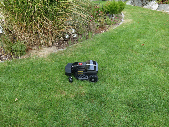 Das Bild zeigt den schwarzen Mähroboter Techline ZR aus der Vogelperspektive, wie er auf einer Gartenwiese steht. Räder sind eingeschlagen zum wenden.
