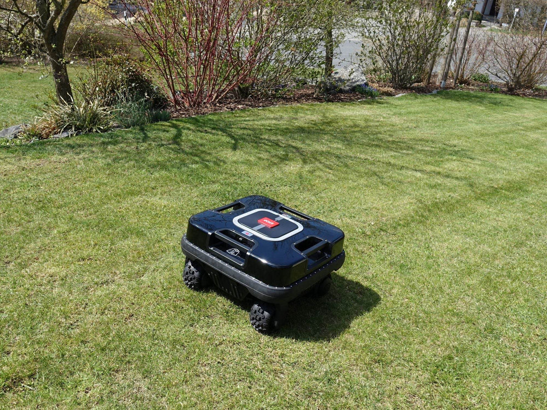 Das Bild zeigt den schwarzen Mähroboter Quadritech aus der Vogelperspektive, wie er einen Abhang hinunterfährt und dabei mäht. Die Aufnahme unterstreicht die Geländetauglichkeit und Effizienz des Geräts, selbst bei unebenen Flächen.