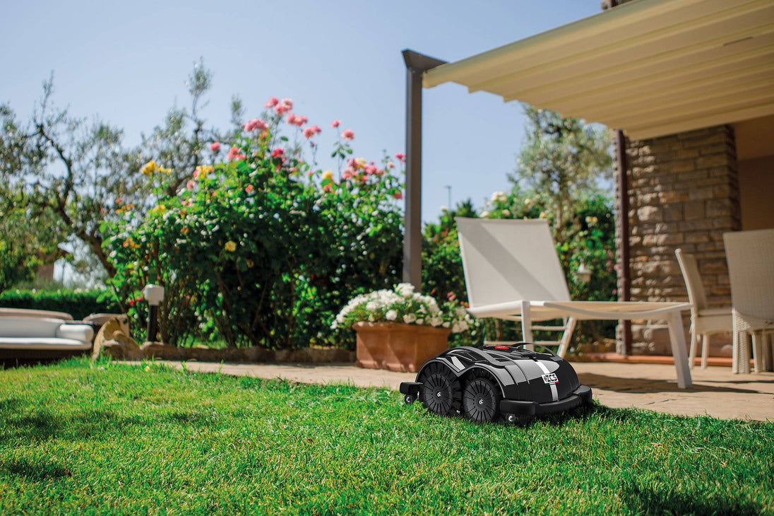 Das Bild zeigt den schwarzen Mähroboter Techline S6, der vor einer Terrasse steht und den Rasen mäht. 
Die Terrasse im Hintergrund verleiht der Szene einen häuslichen und praktischen Charakter, der die Einsatzmöglichkeiten des Geräts im Garten unterstreicht.