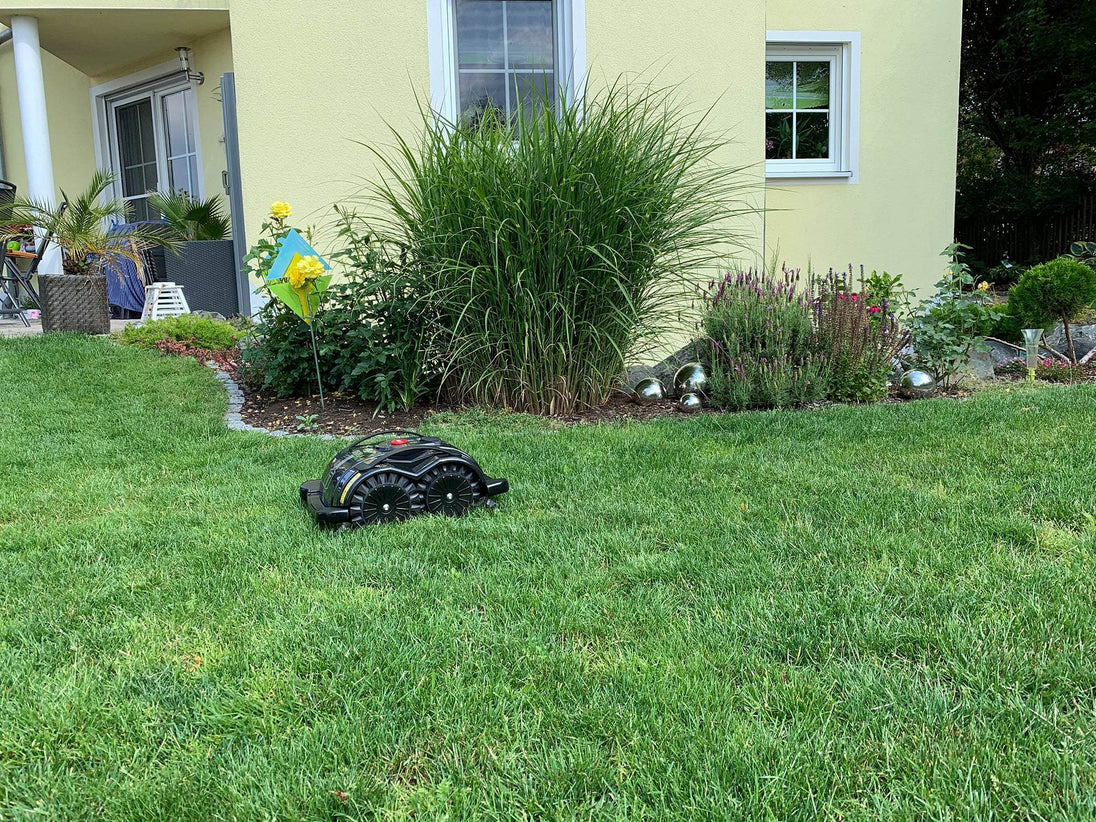 Das Bild zeigt den schwarzen Mähroboter Techline S6, der vor einer Terrasse steht und den Rasen mäht.